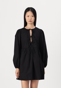 Vestido preto em algodão, com mangas bufantes longas, um decote em forma de chave profundo com laços, e uma cintura franzida para adicionar volume.