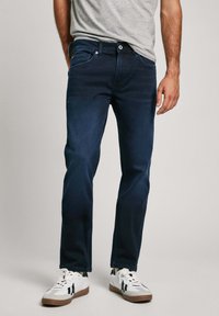 Tumesinised teksad sirge lõikega, varustatud tõmbluku ja nööbiga, viie taskuga ning kergete pleekimisdetailidega. Kombineeritud valgete tossudega.