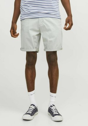 Pantalones cortos de algodón gris claro con dobladillos enrollados, llevados sobre calcetines blancos y zapatillas de deporte azul marino, combinados con una camiseta de rayas horizontales.