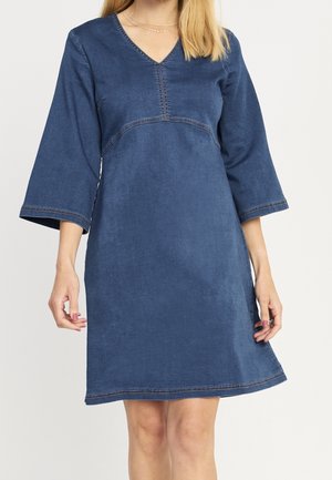 Femme portant une robe en denim bleu foncé au genou, manches trois-quarts et col en V.