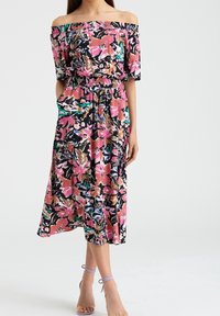 Robe fleurie décolletée avec des motifs roses, noirs et verts, taille smockée, longueur au genou, tissu fluide et manches courtes.