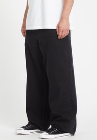 Sorte vide bukser laget av denim, med avslappet passform og minimal søm, parret med svarte kanvas sneakers.