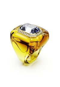 Un anillo amarillo robusto presenta una gran piedra clara en forma de octágono, rodeada de pequeñas gemas brillantes, sobre un fondo blanco.