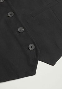 Gros plan d'un tissu noir avec trois boutons ronds noirs et un détail de poche cousu en haut à droite.