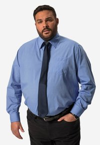 Lichtblauw overhemd met lange mouwen en een borstzak, gecombineerd met een donkere das en zwarte broek. Het overhemd heeft een gladde textuur en een geknopt kraag.