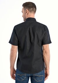 Maglietta nera a maniche corte con colletto strutturato, dettaglio di piega sul retro e texture liscia. Abbinata a jeans blu con cuciture a contrasto.