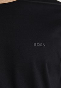 Schwarzes Kurzarmshirt aus glattem Stoff. Es hat einen runden Ausschnitt und ein dezentes erhabenes "BOSS"-Logo auf der Brust in passendem Schwarz.