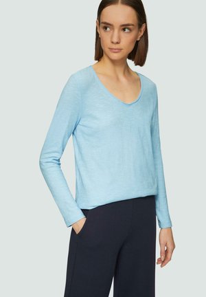 Top azzurro chiaro a maniche lunghe con scollatura a V, texture morbida e vestibilità rilassata, abbinato a pantaloni scuri.
