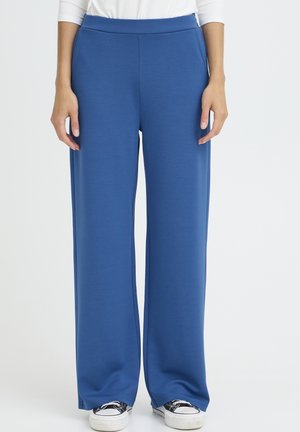 Blaue, weit geschnittene Hosen aus weichem, leichtem Stoff. Sie verfügen über einen elastischen Bund und reichen bis zum Knöchel, kombiniert mit lässigen Sneakers.