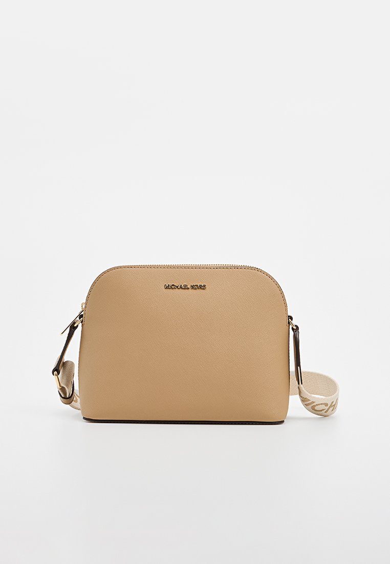 Sac à bandoulière beige en cuir texturé, de forme arrondie, avec un détail logo doré et une sangle contrastante comportant une marque imprimée.