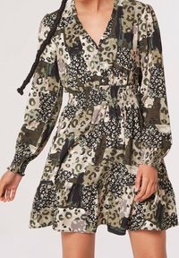 Robe à manches longues avec taille élastique verte, noire, beige et motif léopard abstrait blanc portée par une personne aux cheveux tressés.