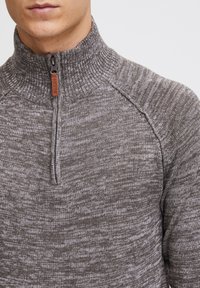 Mock neck genser i en teksturert grå strikk, med glidelås i kvart lengde, ribbestrikket krage og en liten lærdetalj på glidelåsen.