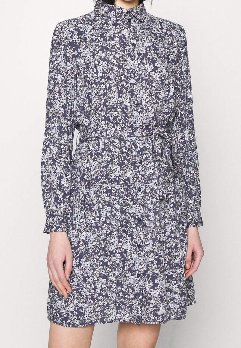 Abito floreale con fondo blu navy, dotato di colletto, maniche lunghe e vita con cintura. Realizzato in tessuto leggero con una texture morbida.