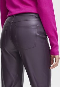 Tætsiddende lilla læderbukser med baglommer og en glat overflade, parret med en lys pink sweater.
