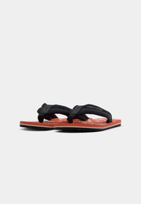 Pair of red flip-flops with white floral pattern and black fabric straps featuring Tommy Hilfiger logo on a white background.