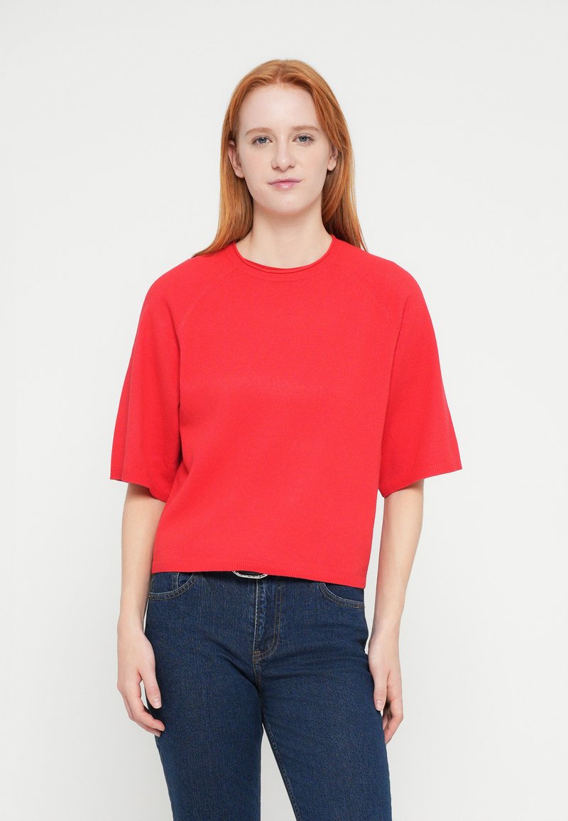 Red cropped knit top with short sleeves, round neckline, and ribbed detailing. Paired with dark blue fitted jeans.
