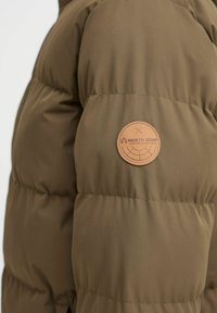 Olivenfarget puffjakke med kviltet design, som har en strukturert overflate og et rundt, brunt skinnmerke merket "North Bend" på ermet.