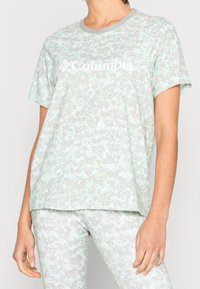 Ljusblå t-shirt med kort ärm och ett prickigt mönster i nyanser av grått, med rund halsringning och Columbia-logotypen i vitt.