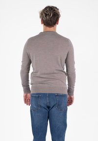 Maglione marrone a maniche lunghe realizzato in materiale morbido, con scollatura rotonda e polsini a costine, abbinato a jeans in denim blu.