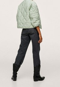 Lysegrøn quilted jakke med en boxy pasform og rund hals, parret med mørkegrå højtaljede jeans og sorte ankelstøvler.