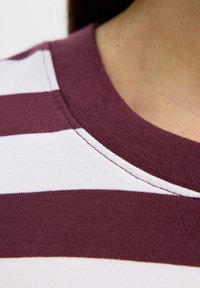 Primo piano del collo di una maglia a righe bordeaux e bianche sul collo e sulla spalla di una persona.