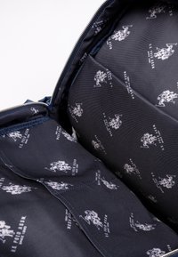 Interno blu navale di una borsa con un motivo a logo bianco ripetuto, texture liscia e chiusura con zip, mostrando la fodera e la struttura.