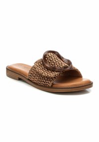 Sandalia deslizante tejida en marrón con un gran acento circular, plantilla de piel suave en tono beige y un bajo tacón de madera. Presenta un diseño superior texturizado.