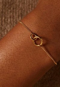 Gouden armband met twee verbonden ovale ringen, bevestigd aan een delicate ketting met een gladde textuur.