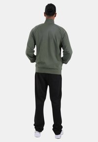 Felpa verde con collo alto, maniche raglan, e pantaloni della tuta neri con polsini elastici, indossata con sneakers bianche. Design semplice senza motivi.