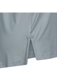 Camisa gris claro con una textura suave, que presenta aberturas laterales en el dobladillo y costuras bien terminadas. Diseño simple y funcional.