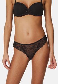 Conjunto de lencería de encaje negro que incluye un sujetador balconette con un diseño floral y un tanga a juego. La tela es transparente y tiene bordes festoneados.