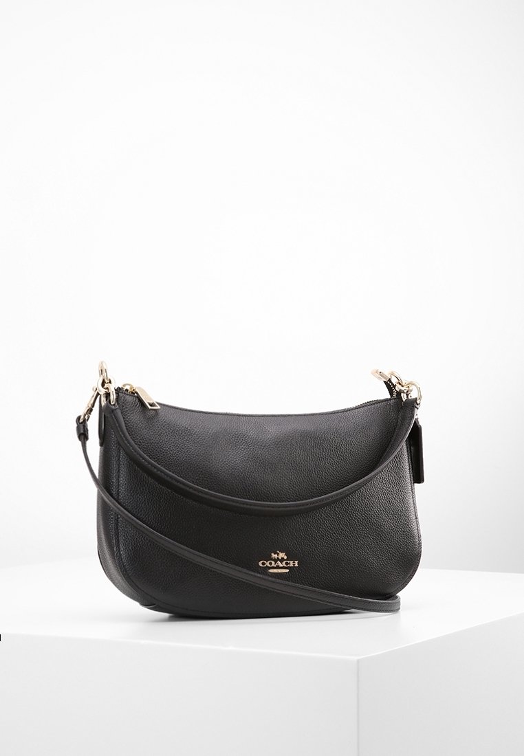 Sac à main en cuir noir Coach avec logo doré et bandoulière détachable présenté sur une surface blanche.