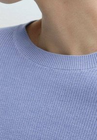 Jasnoniebieski sweter z teksturowanym dzianym wzorem, z prążkowanym dekoltem, prezentujący równomierny wzór na całej tkaninie. Zbliżenie na obszar kołnierza.