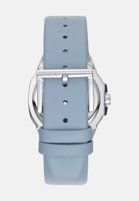 Zilveren horloge met een ronde wijzerplaat, lichtblauwe leren strap en gepolijste sluiting. De strap heeft meerdere gaten voor aanpassing en een gladde textuur.