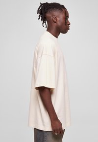 Krém színű, oversized póló, rövid ujjú, kerek nyakú, sima textúrával, elnyűtt farmernadrággal párosítva. Egyszerű és modern dizájn.