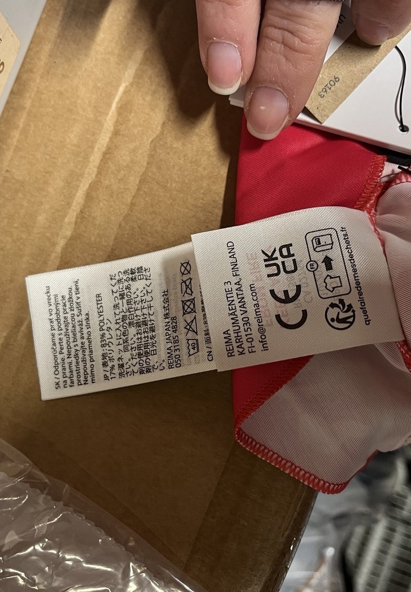 Étiquette en tissu rouge attachée à un vêtement, affichant les instructions d'entretien, la composition du matériau (polyester) et les informations sur la marque.