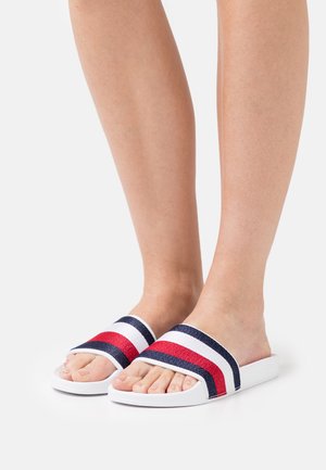 Białe klapki z trzema wyraźnymi paskami: czerwonym, granatowym i białym. Gładki materiał z szerokim paskiem i płaską podeszwą. Widoczne palce.