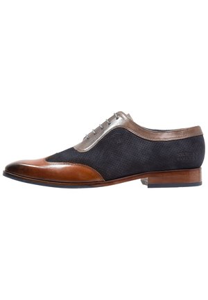 Herrenschuh aus braunem Leder und schwarzem Veloursleder mit Flügelkappe, Schnürverschluss und niedrigem Holzabsatz.