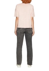 Koszulka z krótkim rękawem w jasnoróżowym kolorze z okrągłym dekoltem, zestawiona z ciemnoszarymi dżinsami z tylnymi kieszeniami i prostym krojem.
