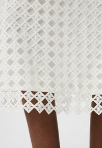 Jupe blanche avec un design en treillis de diamant. Présente des accents brodés le long de l'ourlet, mettant en valeur une texture et un motif complexes.