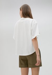 Camiseta blanca de manga corta con un corte relajado, fabricada en suave algodón y con cuello redondo, combinada con pantalones cortos de color verde olivo.