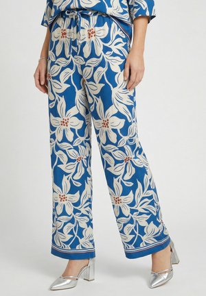 Blaue Hose mit großem weißem Blumenmuster, Kordelzugbund, getragen mit silbernen Schuhen mit Blockabsatz.