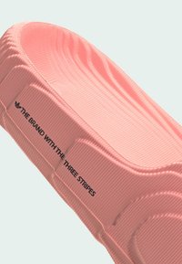 Rosa Gummischuh zum Hineinschlüpfen mit geriffelter Textur, versehen mit schwarzem Markentext. Das gebogene Design und die glatten Kanten betonen die Funktionalität.