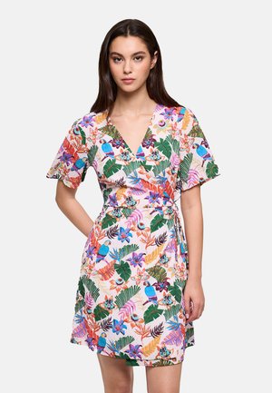 Mujer con un vestido cruzado de manga corta con un estampado tropical colorido de flores y aves sobre un fondo blanco.