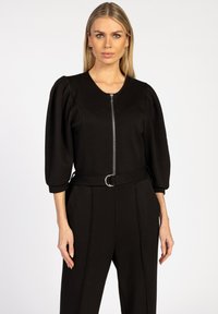 Zwarte zip-up top met puffed korte mouwen, een aansluitende silhoeet en een bijpassende riem met een zilveren cirkelvormige gesp. Gladde textuur.