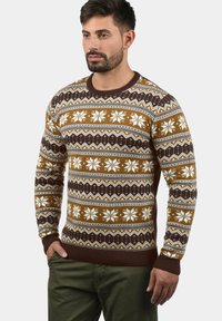 Brun och krämfärgad mönstrad tröja med snöflinge-design, stickad textur och ribbade manschetter och nederkant. Bärs med olivgröna byxor.