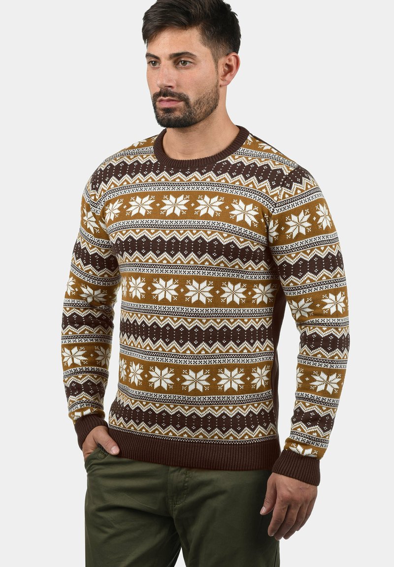 Brun och krämfärgad mönstrad tröja med snöflinge-design, stickad textur och ribbade manschetter och nederkant. Bärs med olivgröna byxor.