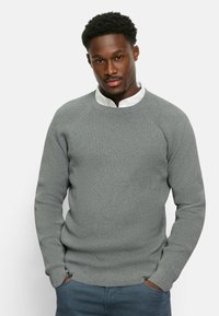 Helles graues, strukturiertes Sweatshirt mit gerippten Bündchen und Saum, getragen über einem weißen Hemd mit Kragen. Gerade geschnitten mit lockerer Passform und Rundhalsausschnitt.
