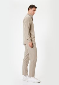 Beige strikket sweater med høj krave, parret med lyse beige bukser og hvide sneakers. Glat tekstur og tætsiddende design.