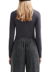 Langärmliges, dunkelgraues Oberteil mit glatter Textur, kombiniert mit hochgeschnittenen, schwarz-weißen Tweed-Hosen mit elastischem Bund.